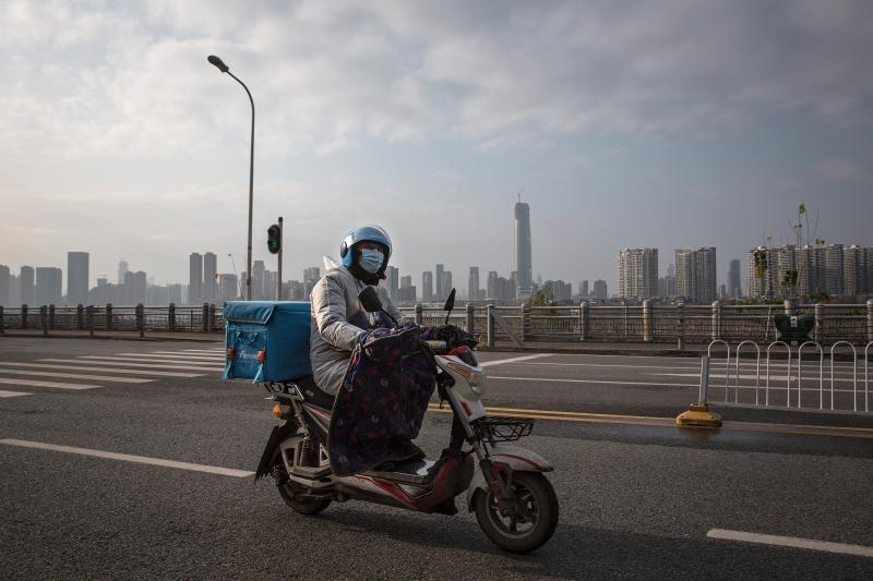 A delivery worker on a motorcycle on an empty street in Wuhan. Despite the city's lockdown measures to prevent the spread of disease, a handful of delivery companies are still in operation. Their workers provide supplies and necessities to residents coope A delivery worker on a motorcycle on an empty street in Wuhan. Despite the city's lockdown measures to prevent the spread of disease, a handful of delivery companies are still in operation. Their workers provide supplies and necessities to residents coope