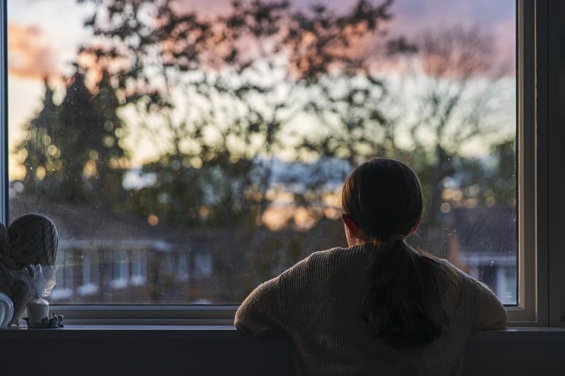 A girl looks out of her bedroom window as the sun is setting. A girl looks out of her bedroom window as the sun is setting.