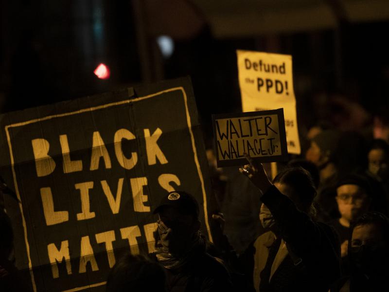 Demonstrators hold placards reading "BLACK LIVES MATTER," "Walter Wallace JR." and DEFUND PPD" as they gather in protest near the location where Wallace, a 27-year-old Black man, was killed by two police officers in Philadelphia. Police officers said he w Demonstrators hold placards reading "BLACK LIVES MATTER," "Walter Wallace JR." and DEFUND PPD" as they gather in protest near the location where Wallace, a 27-year-old Black man, was killed by two police officers in Philadelphia. Police officers said he w