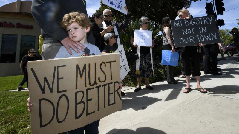 Kyle Fox, 4, and his father Brady Fox hold a sign at a Sunday vigil held to support the Chabad of Poway synagogue. A teenager opened fire at the synagogue near San Diego on Saturday, killing one and injuring three others. Kyle Fox, 4, and his father Brady Fox hold a sign at a Sunday vigil held to support the Chabad of Poway synagogue. A teenager opened fire at the synagogue near San Diego on Saturday, killing one and injuring three others.