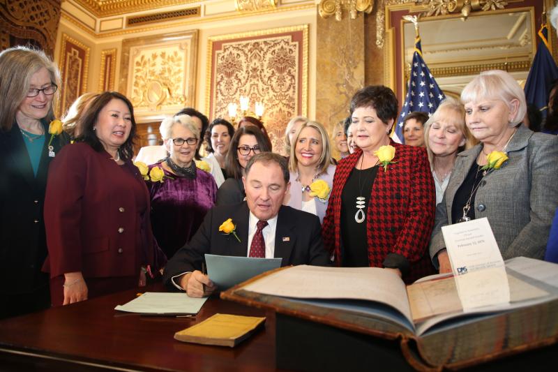 Utah Gov. Gary Herbert signs bill honoring the state's pioneering women suffragists on Wednesday. He's surrounded by state senators and representatives, and his wife, who are all wearing the yellow rose symbolizing suffrage. Utah Gov. Gary Herbert signs bill honoring the state's pioneering women suffragists on Wednesday. He's surrounded by state senators and representatives, and his wife, who are all wearing the yellow rose symbolizing suffrage.
