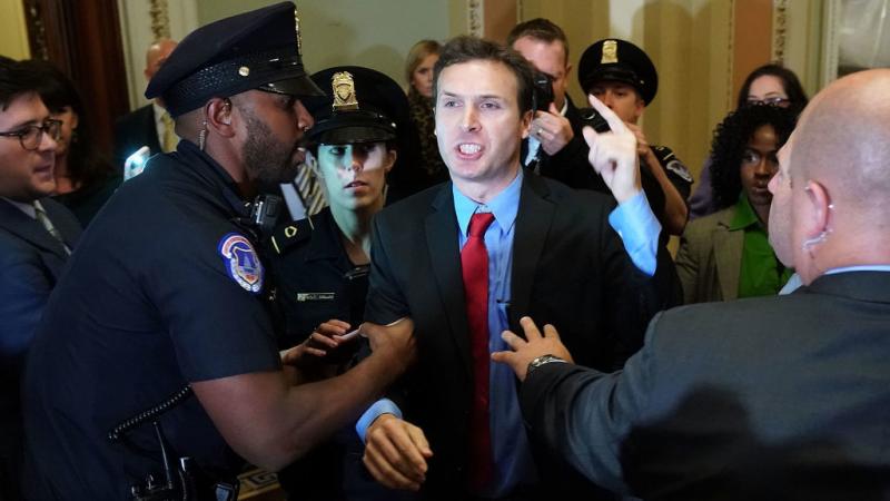 Ryan Clayton of Americans Take Action is corralled by police after he threw Russian flags at Senate Majority Leader Mitch McConnell and President Trump as they arrived for the Republican Senate Policy Luncheon at the Capitol. Ryan Clayton of Americans Take Action is corralled by police after he threw Russian flags at Senate Majority Leader Mitch McConnell and President Trump as they arrived for the Republican Senate Policy Luncheon at the Capitol.