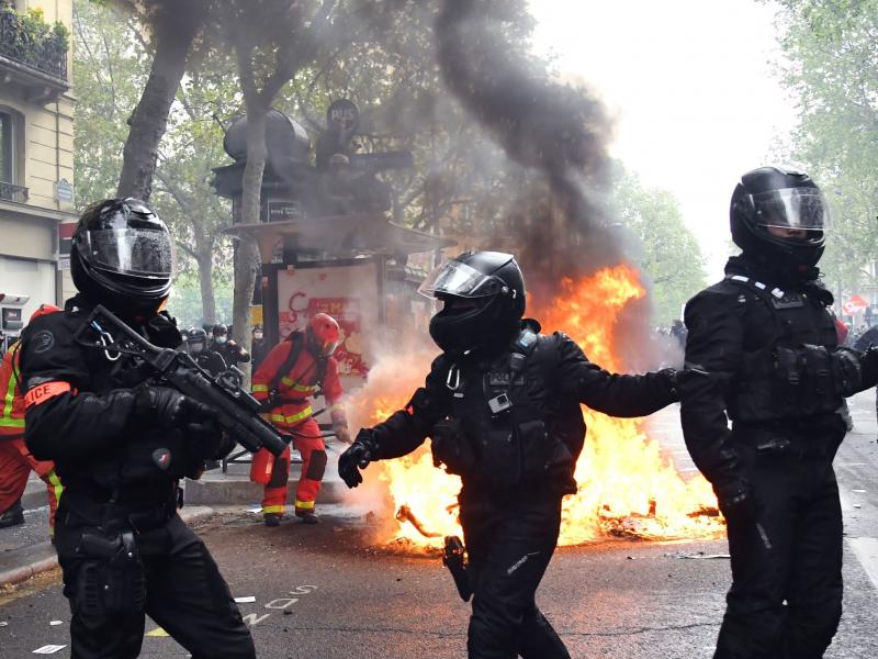 Police officers walk near a fire burning in the street during May Day protests in Paris on Saturday. Police officers walk near a fire burning in the street during May Day protests in Paris on Saturday.