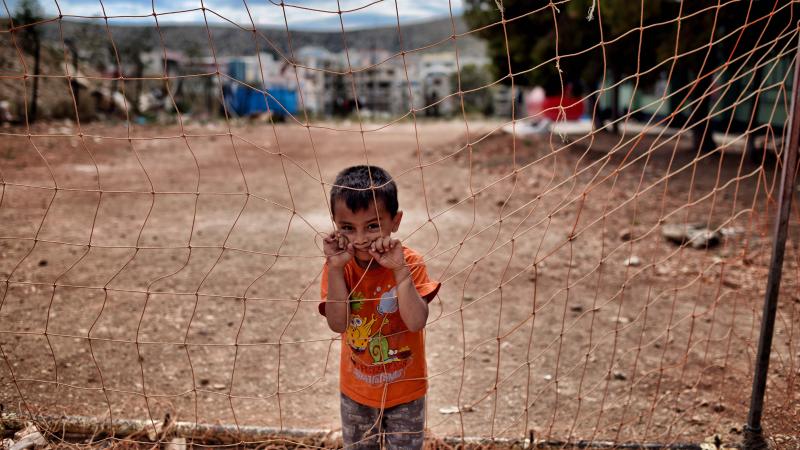 A boy looks on behind a net at the refugee camp of Schisto in Athens, Greece, on June 8. A boy looks on behind a net at the refugee camp of Schisto in Athens, Greece, on June 8.