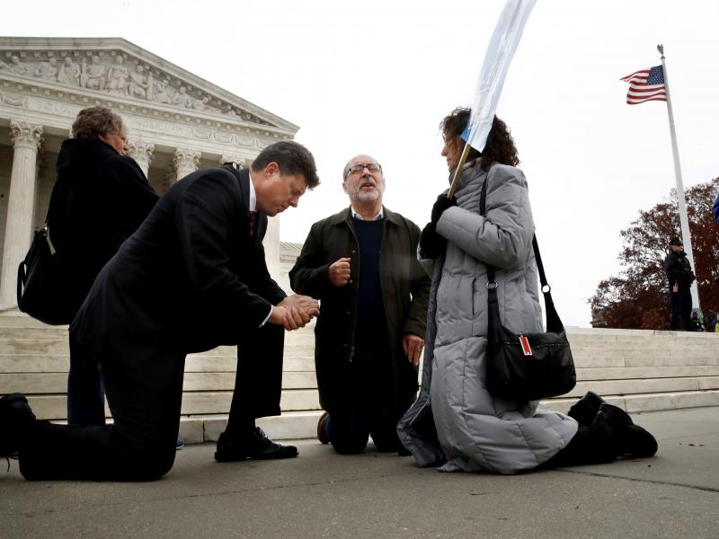 The Rev. Brad Wells, left, the Rev. Patrick Mahoney and Paula Oas, kneel in prayer in front of the Supreme Court, as the court hears the Masterpiece Cakeshop case. The Rev. Brad Wells, left, the Rev. Patrick Mahoney and Paula Oas, kneel in prayer in front of the Supreme Court, as the court hears the Masterpiece Cakeshop case.