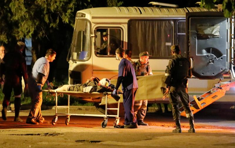 A wounded service member of the Ukrainian forces from the besieged Azovstal steel mill in Mariupol is transported out of a bus on a stretcher under escort of pro-Russian fighters, upon arrival in Novoazovsk, Ukraine, on Monday. A wounded service member of the Ukrainian forces from the besieged Azovstal steel mill in Mariupol is transported out of a bus on a stretcher under escort of pro-Russian fighters, upon arrival in Novoazovsk, Ukraine, on Monday.