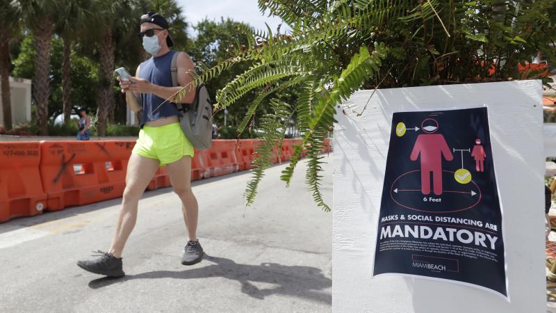 A pedestrian in a mask passes a sign urging people to practice social distancing, on Saturday in Miami Beach, Fla. Just as residents flocked outside to enjoy the Fourth of July, states such as Florida were reporting skyrocketing numbers of confirmed coron A pedestrian in a mask passes a sign urging people to practice social distancing, on Saturday in Miami Beach, Fla. Just as residents flocked outside to enjoy the Fourth of July, states such as Florida were reporting skyrocketing numbers of confirmed coron
