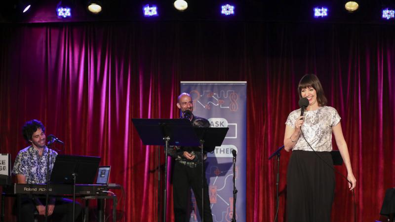 Ask Me Another host Ophira Eisenberg performs on stage alongside guest musician Julian Velard and guest announcer Cecil Baldwin at the Bell House in Brooklyn, New York. Ask Me Another host Ophira Eisenberg performs on stage alongside guest musician Julian Velard and guest announcer Cecil Baldwin at the Bell House in Brooklyn, New York.