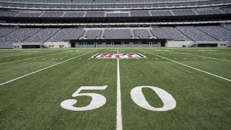 The NFL logo on the 50-yard line at an empty NFL stadium. The NFL logo on the 50-yard line at an empty NFL stadium.