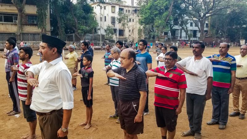 Members of the Rashtriya Swayamsevak Sangh, or RSS, stand at attention and salute a saffron-orange flag at a morning shakha, or drill session, in a park in suburban Mumbai, India. Members of the Rashtriya Swayamsevak Sangh, or RSS, stand at attention and salute a saffron-orange flag at a morning shakha, or drill session, in a park in suburban Mumbai, India.