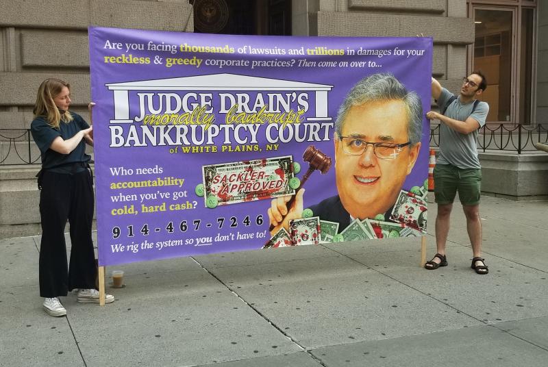 Two demonstrators protest against U.S. Judge Robert Drain, who has granted immunity from future opioid lawsuits to members of the Sackler family. Two demonstrators protest against U.S. Judge Robert Drain, who has granted immunity from future opioid lawsuits to members of the Sackler family.