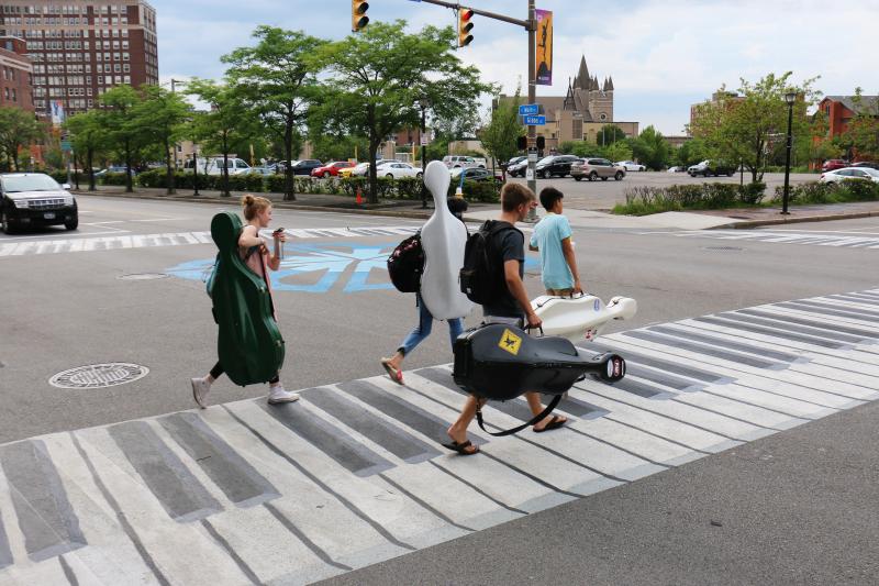 Musicians walk on a crosswalk painted like a piano outside the Eastman School of Music in Rochester, N.Y. Increasingly, urban designers and transportation planners say this kind of art — colorful crosswalks and engaging sidewalks — leads to safer inte Musicians walk on a crosswalk painted like a piano outside the Eastman School of Music in Rochester, N.Y. Increasingly, urban designers and transportation planners say this kind of art — colorful crosswalks and engaging sidewalks — leads to safer inte