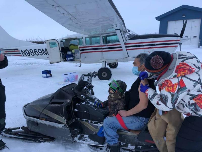 Sarah Lind, a nurse with Yukon-Kuskokwim Health Corp., Southwest Alaska's tribal health care provider, vaccinates James Evan in December. They're standing on the tarmac in the village of Napakiak, where Evan works for YKHC at the clinic. Sarah Lind, a nurse with Yukon-Kuskokwim Health Corp., Southwest Alaska's tribal health care provider, vaccinates James Evan in December. They're standing on the tarmac in the village of Napakiak, where Evan works for YKHC at the clinic.