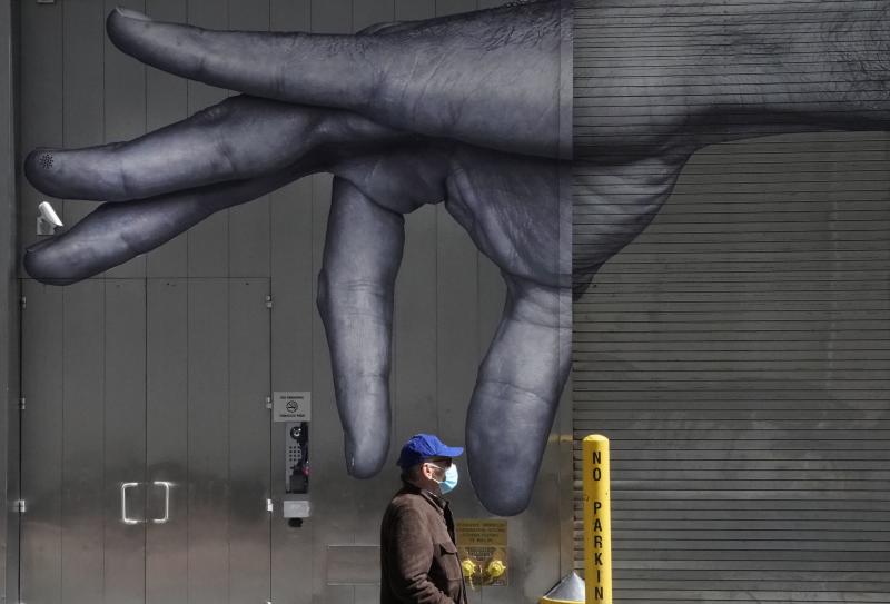 A man in a mask walks past a mural on the side of a building in New York City in April. A man in a mask walks past a mural on the side of a building in New York City in April.