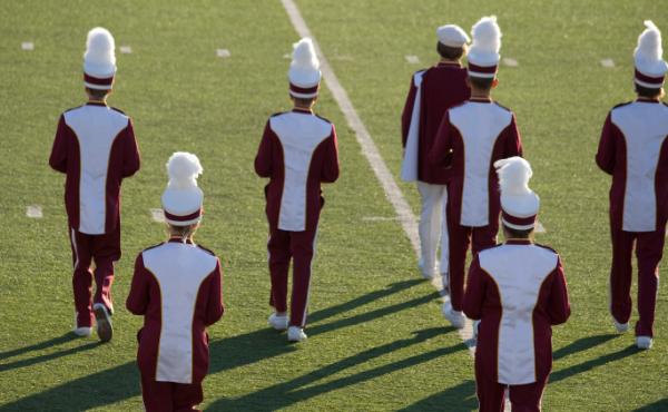 A marching band performs at halftime on the field during a high school football game. A marching band performs at halftime on the field during a high school football game.