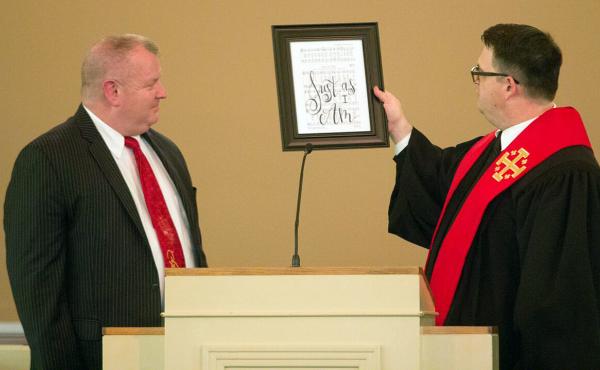 Nick Wilson (left), at his ordination last month, is given a framed sign from Pastor Matt Johnson that reads "Just As I Am," the title of one of Wilson's favorite hymns. Nick Wilson (left), at his ordination last month, is given a framed sign from Pastor Matt Johnson that reads "Just As I Am," the title of one of Wilson's favorite hymns.