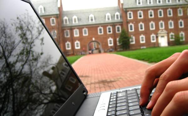 A student works on a laptop on a college quad. A student works on a laptop on a college quad.