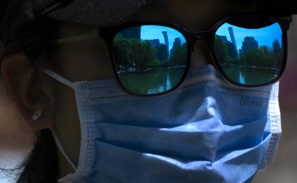The skyline of Beijing is reflecting in the sunglasses of a woman wearing a face mask as she walks at a public park in Beijing, Thursday, April 14, 2022. The skyline of Beijing is reflecting in the sunglasses of a woman wearing a face mask as she walks at a public park in Beijing, Thursday, April 14, 2022.