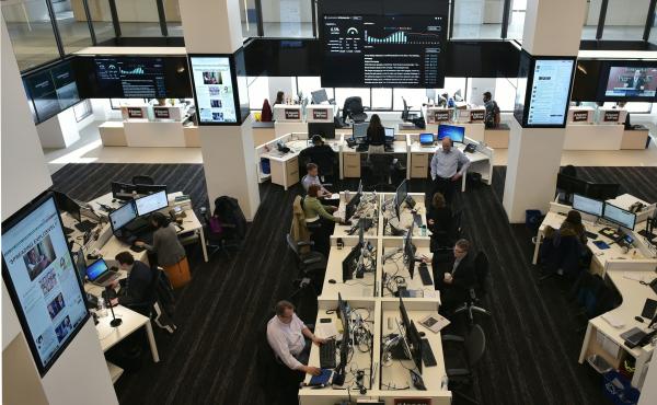 Journalists at The Washington Post work in a newsroom surrounded by screens showing its website and updated reader metrics. Journalists at The Washington Post work in a newsroom surrounded by screens showing its website and updated reader metrics.