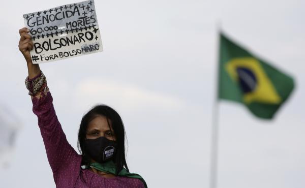 A women's movement activist holds a sign that reads in Portuguese "Genocide 60 thousand deaths, Bolsonaro out," during a protest against the government's handling of the pandemic earlier this month. A women's movement activist holds a sign that reads in Portuguese "Genocide 60 thousand deaths, Bolsonaro out," during a protest against the government's handling of the pandemic earlier this month.