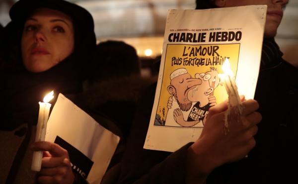 A man holds a cartoon published by Charlie Hebdo during a gathering at Republic Square in Paris on Wednesday, to show solidarity for victims of the attack on the offices of the satirical weekly. A man holds a cartoon published by Charlie Hebdo during a gathering at Republic Square in Paris on Wednesday, to show solidarity for victims of the attack on the offices of the satirical weekly.