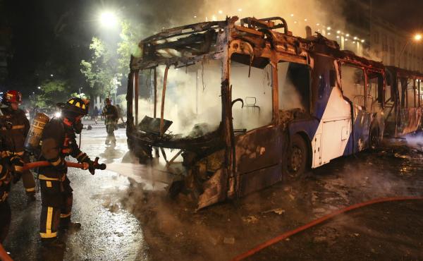 Firefighters put out the flames on a burning bus during a protest against the rising cost of subway and bus fares in Santiago, Chile. Firefighters put out the flames on a burning bus during a protest against the rising cost of subway and bus fares in Santiago, Chile.