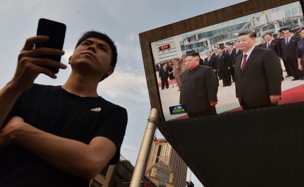 A man waits for a taxi in Beijing as news footage of Chinese President Xi Jinping (right) being greeted in Pyongyang by North Korean leader Kim Jong Un is shown on a large screen outside a shopping mall. A man waits for a taxi in Beijing as news footage of Chinese President Xi Jinping (right) being greeted in Pyongyang by North Korean leader Kim Jong Un is shown on a large screen outside a shopping mall.