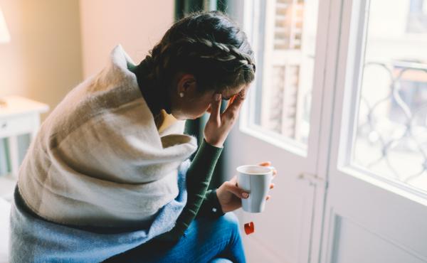 A woman with a temperature stays home, wrapped in a scarf while drinking hot tea. A woman with a temperature stays home, wrapped in a scarf while drinking hot tea.