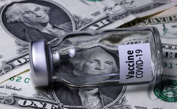 A COVID-19 vaccine vial sits on top of dollar bills. A COVID-19 vaccine vial sits on top of dollar bills.