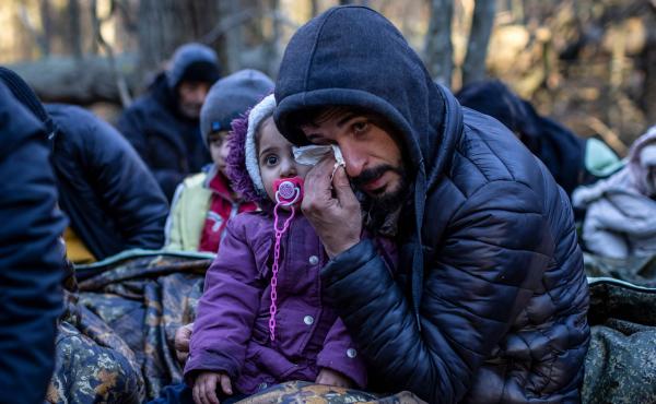 A man holding a child wipes his eye as the Kurdish family from Dohuk in Iraq waits for the border guard patrol, near Narewka, Poland, near the Polish-Belarusian border on Nov. 9. The three-generation family of 16 — with seven minors, including the young A man holding a child wipes his eye as the Kurdish family from Dohuk in Iraq waits for the border guard patrol, near Narewka, Poland, near the Polish-Belarusian border on Nov. 9. The three-generation family of 16 — with seven minors, including the young