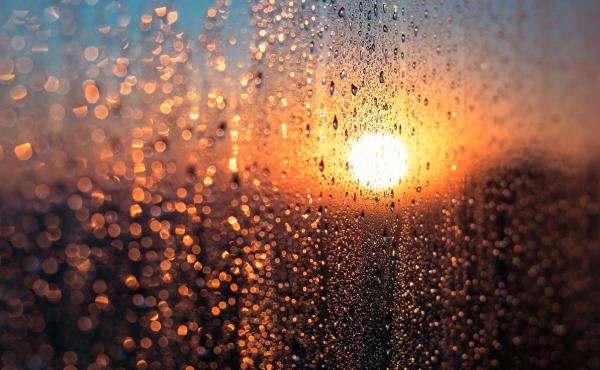 A wet window with condensation set against the sun's glow A wet window with condensation set against the sun's glow