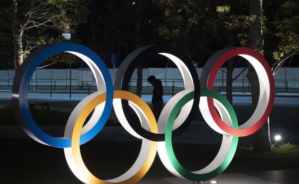 A man is seen through the Olympic rings in front of the New National Stadium in Tokyo, on Tuesday. The Summer Games have been delayed amid the coronavirus pandemic. A man is seen through the Olympic rings in front of the New National Stadium in Tokyo, on Tuesday. The Summer Games have been delayed amid the coronavirus pandemic.