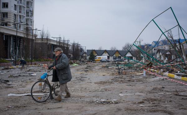 A man walks his bike through a parking lot littered with broken glass in Bucha, Ukraine. A man walks his bike through a parking lot littered with broken glass in Bucha, Ukraine.