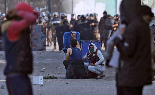 Iraqi demonstrators take cover from security forces behind trash cans during clashes in the city of Karbala on Thursday. Iraqi demonstrators take cover from security forces behind trash cans during clashes in the city of Karbala on Thursday.