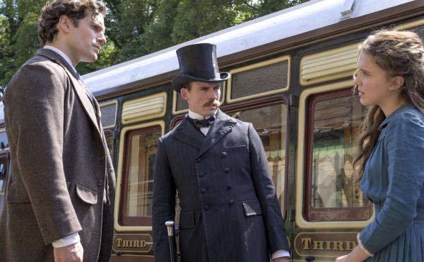 "The train's afoot!": (L to R) Sherlock (Henry Cavill) and Mycroft (Sam Claflin) literally look down on their younger sister Enola (Millie Bobby Brown) in Netflix's Enola Holmes. "The train's afoot!": (L to R) Sherlock (Henry Cavill) and Mycroft (Sam Claflin) literally look down on their younger sister Enola (Millie Bobby Brown) in Netflix's Enola Holmes.