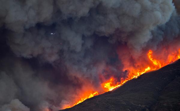 A firefighting helicopter is dwarfed by smoke and flames during Thomas Fire on Thursday. A firefighting helicopter is dwarfed by smoke and flames during Thomas Fire on Thursday.