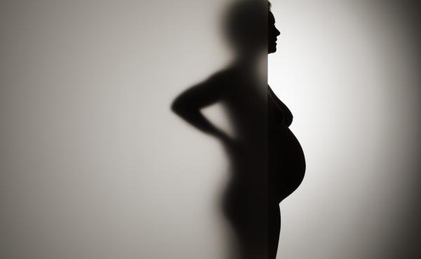 A pregnant woman stands behind frosty glass. A pregnant woman stands behind frosty glass.