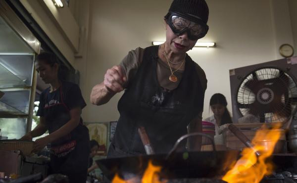 Chef Jay Fai wears a wool cap and safety goggles to ward off the heat from the charcoal fires in the alley where she cooks all of the restaurant's meals. She is such a perfectionist that she doesn't let anyone on her staff do the cooking. Chef Jay Fai wears a wool cap and safety goggles to ward off the heat from the charcoal fires in the alley where she cooks all of the restaurant's meals. She is such a perfectionist that she doesn't let anyone on her staff do the cooking.