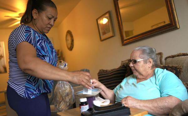 Expanded funds for in-home care can help seniors and disabled Americans stay in their homes. Here, Lidia Vilorio, a home health aide, gives her patient Martina Negron her medicine and crackers for her tea in May in Haverstraw, N.Y. Expanded funds for in-home care can help seniors and disabled Americans stay in their homes. Here, Lidia Vilorio, a home health aide, gives her patient Martina Negron her medicine and crackers for her tea in May in Haverstraw, N.Y.