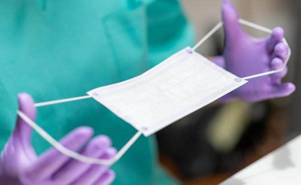 Hands in protective gloves holding stretching bands on protective mask for application. Hands in protective gloves holding stretching bands on protective mask for application.