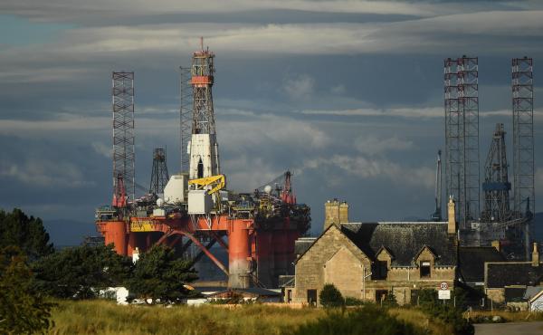 An oil rig towers over houses last week in Nigg, Scotland. Major players in the oil industry expect depressed oil demand and low prices to continue well into next year. An oil rig towers over houses last week in Nigg, Scotland. Major players in the oil industry expect depressed oil demand and low prices to continue well into next year.