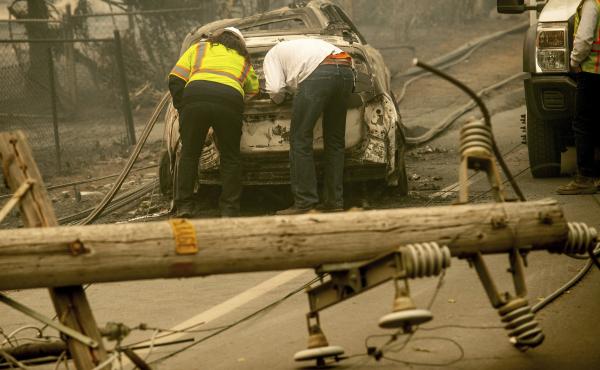 With a downed power utility pole in the foreground, residents of Paradise, Calif., examine a burned-out vehicle destroyed by last year's wildfire. With a downed power utility pole in the foreground, residents of Paradise, Calif., examine a burned-out vehicle destroyed by last year's wildfire.