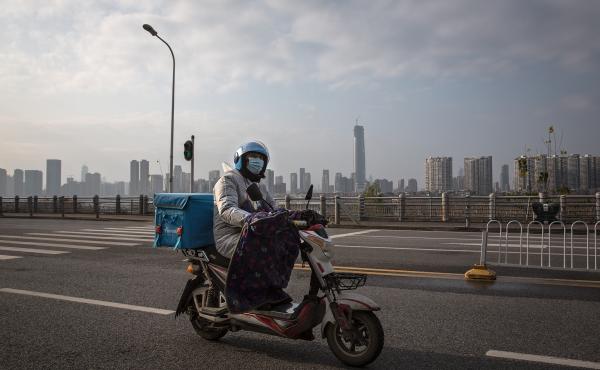 A delivery worker on a motorcycle on an empty street in Wuhan. Despite the city's lockdown measures to prevent the spread of disease, a handful of delivery companies are still in operation. Their workers provide supplies and necessities to residents coope A delivery worker on a motorcycle on an empty street in Wuhan. Despite the city's lockdown measures to prevent the spread of disease, a handful of delivery companies are still in operation. Their workers provide supplies and necessities to residents coope