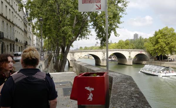 A municipal employee (right) talks to a pedestrian next to a controversial street urinal installed on the Seine river banks of Île de la Cité, Paris, in August. A municipal employee (right) talks to a pedestrian next to a controversial street urinal installed on the Seine river banks of Île de la Cité, Paris, in August.