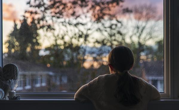 A girl looks out of her bedroom window as the sun is setting. A girl looks out of her bedroom window as the sun is setting.