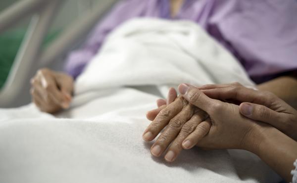A daughter holds her mother's hand and encourages her while sitting on a hospital bed. A daughter holds her mother's hand and encourages her while sitting on a hospital bed.