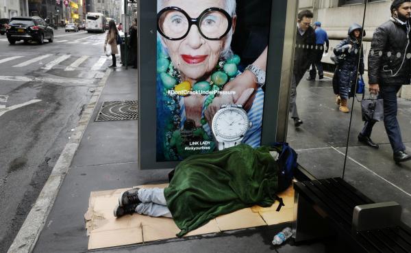 A homeless man sleeps under a blanket in a Fifth Avenue bus shelter in New York. A homeless man sleeps under a blanket in a Fifth Avenue bus shelter in New York.