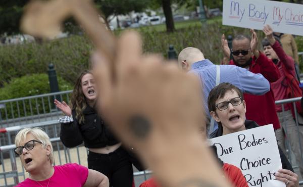 Nate Darnell holds a cross while surrounded by chanting abortion-rights demonstrators outside the U.S. Supreme Court on Thursday in Washington, D.C. Nate Darnell holds a cross while surrounded by chanting abortion-rights demonstrators outside the U.S. Supreme Court on Thursday in Washington, D.C.