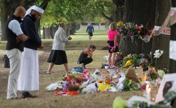 People on Tuesday stand next to floral tributes placed across the road from the Al Noor Mosque in Christchurch, New Zealand, where dozens of worshippers were gunned down last week. People on Tuesday stand next to floral tributes placed across the road from the Al Noor Mosque in Christchurch, New Zealand, where dozens of worshippers were gunned down last week.