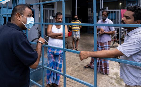 Singapore is seeing a spike in coronavirus cases among its hundreds of thousands of migrant workers. Above, a volunteer from a nonprofit group talks to migrant workers now confined to a factory that was converted to a dormitory as part of the effort to co Singapore is seeing a spike in coronavirus cases among its hundreds of thousands of migrant workers. Above, a volunteer from a nonprofit group talks to migrant workers now confined to a factory that was converted to a dormitory as part of the effort to co